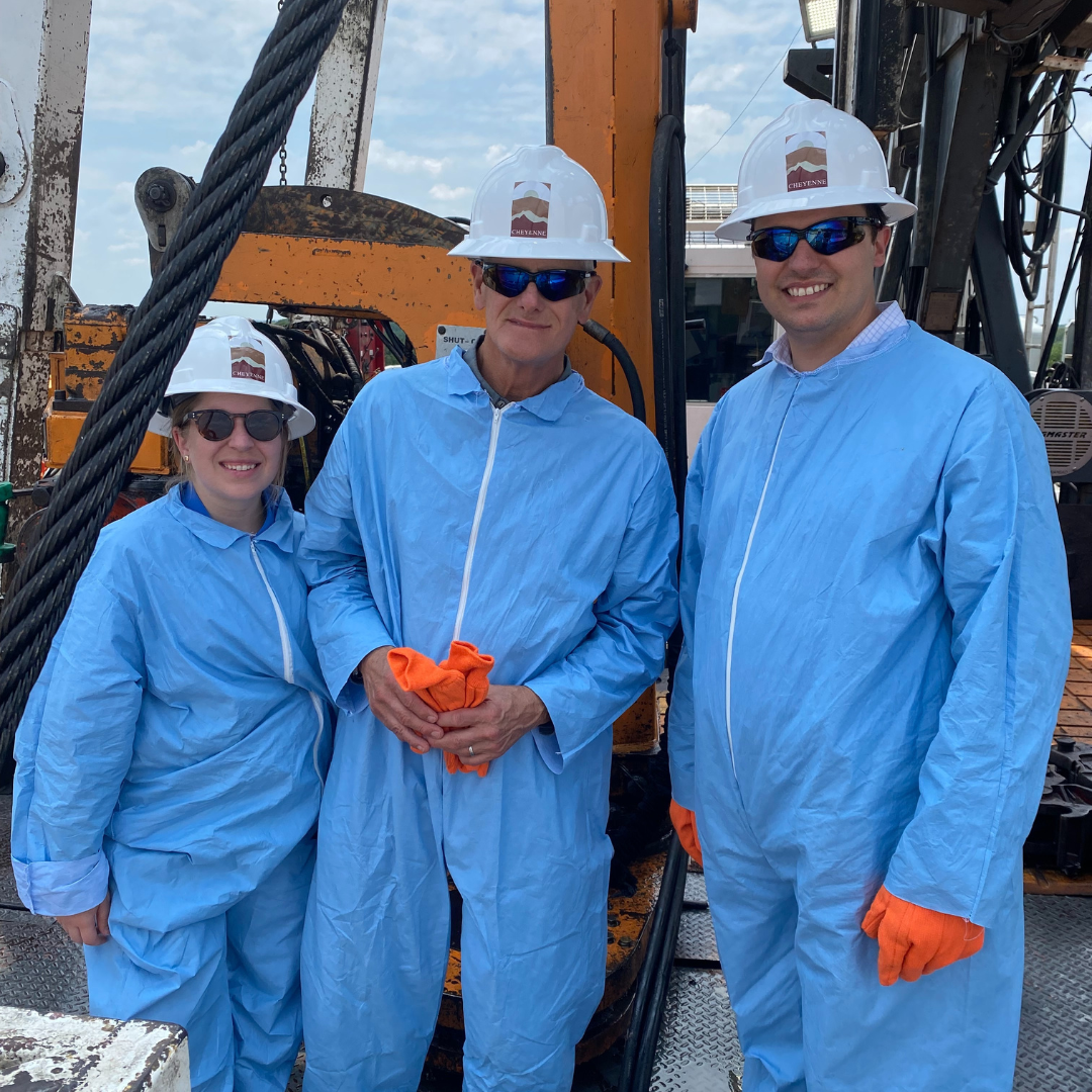 three people in hazard suits and hard hats in front of an oil rig