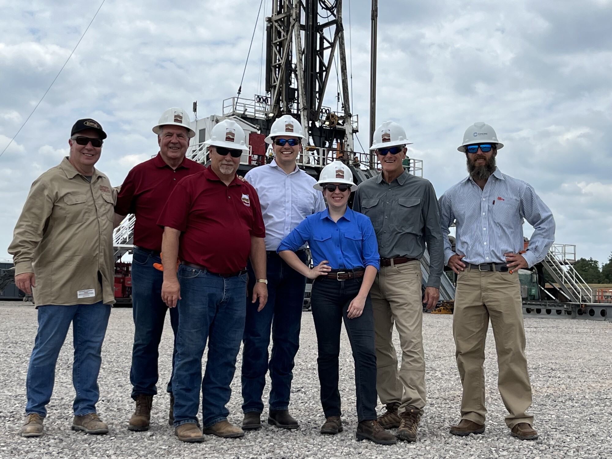 Group of people in hardhats and plain clothes in front of oil rig